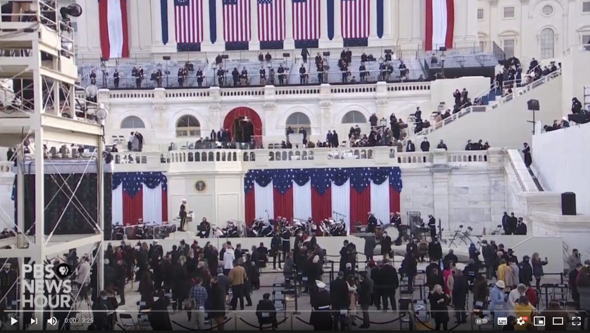 Photo: a news video still from the US Capitol with dignitaries, flags and a band.